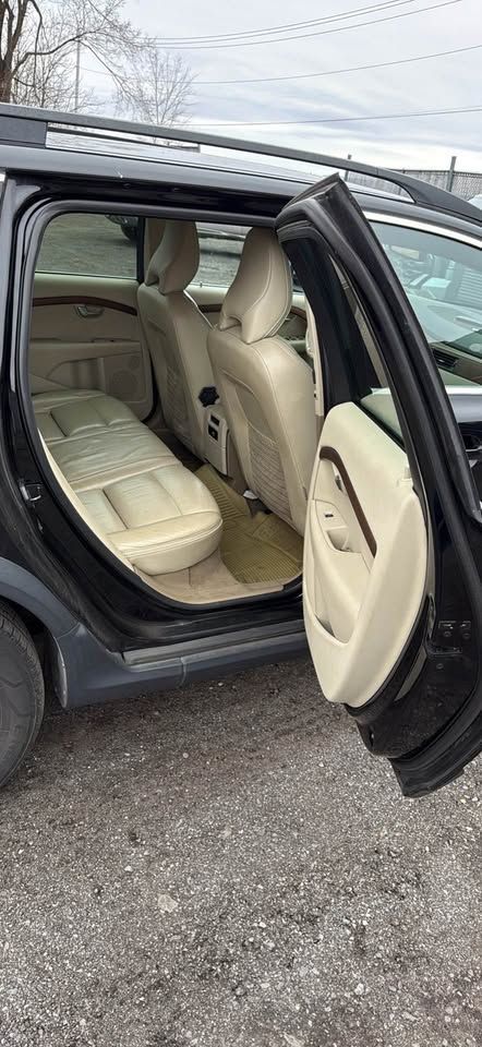 The open rear passenger side door of a dark-colored SUV reveals beige leather seats and interior trim.