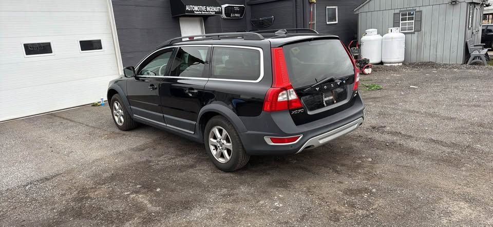 A black Volvo XC70 station wagon parked on a gravel lot in front of a white garage door.