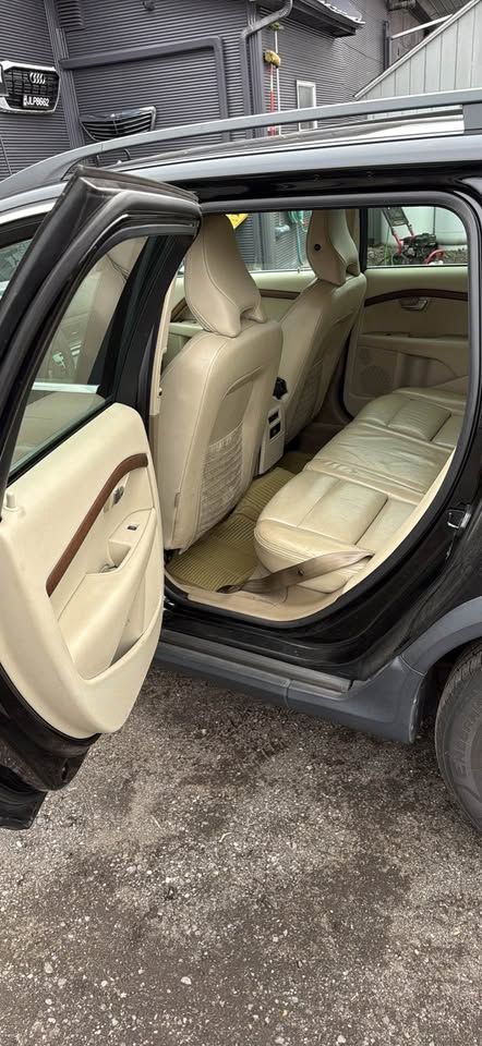 Interior of a car's rear passenger side, showing beige leather seats and door paneling with dark trim, parked outdoors.