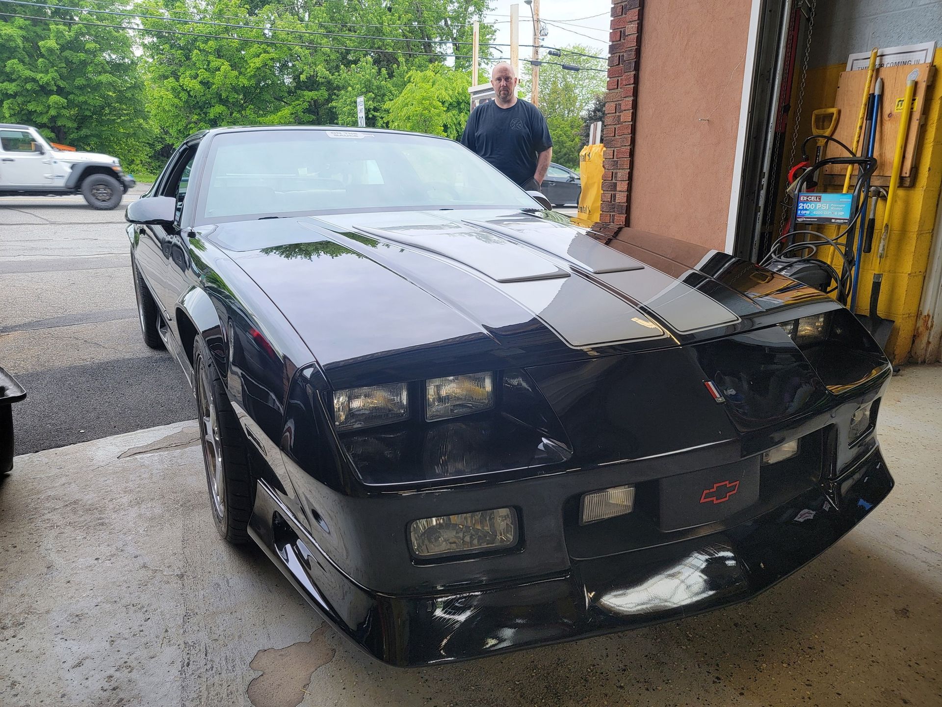 Black Chevrolet Camaro IROC-Z parked outside garage; man in background.