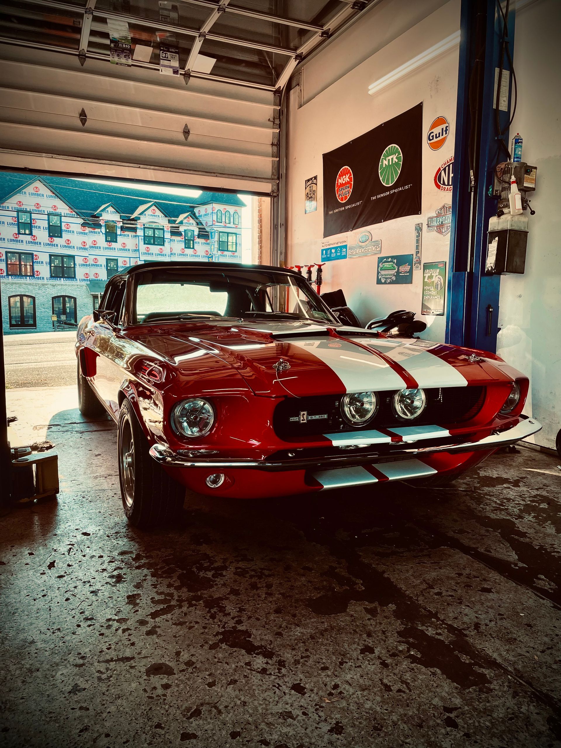 Red and white vintage Shelby Mustang inside a garage with an open door.