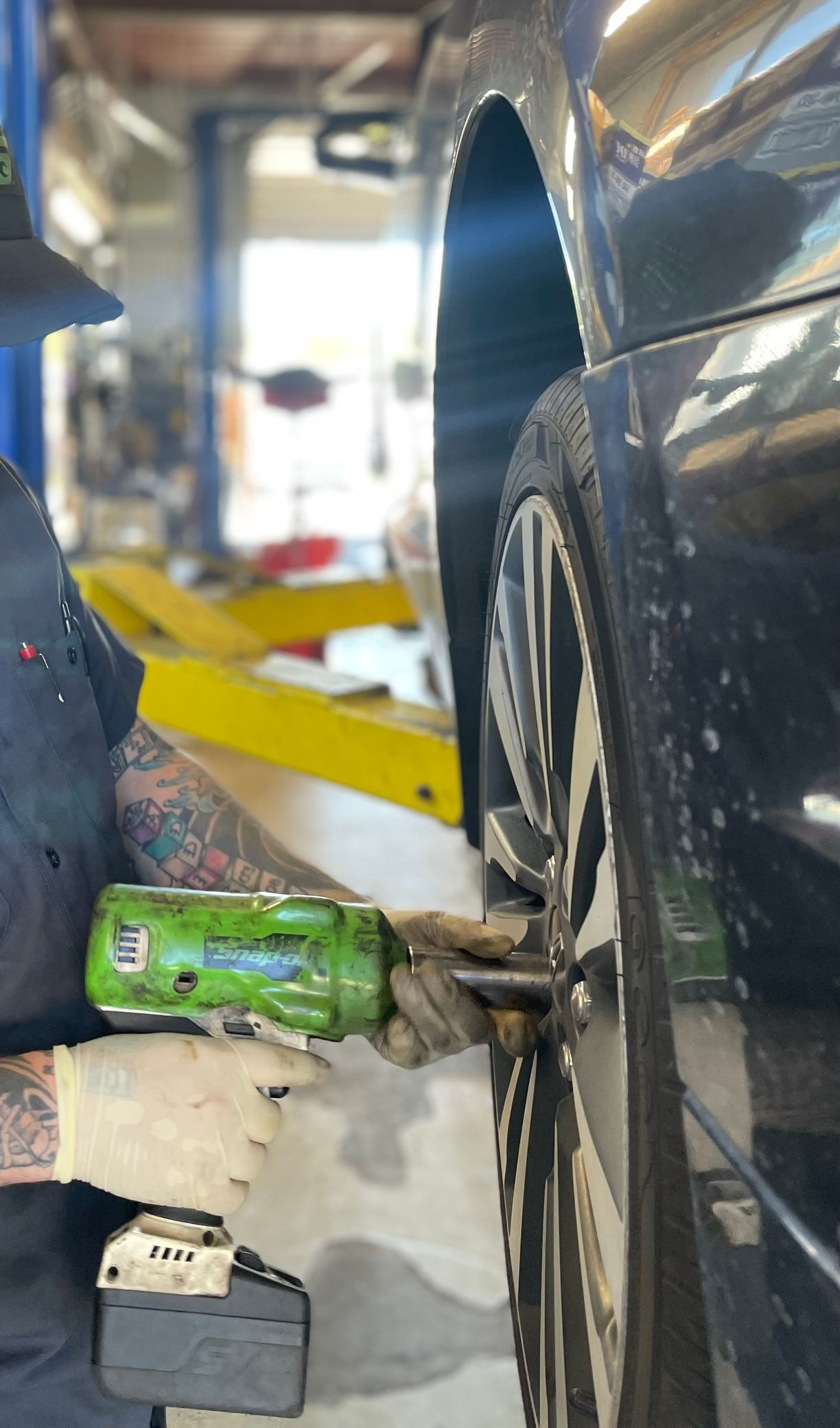 Mechanic using a power tool to remove lug nuts from a car tire.