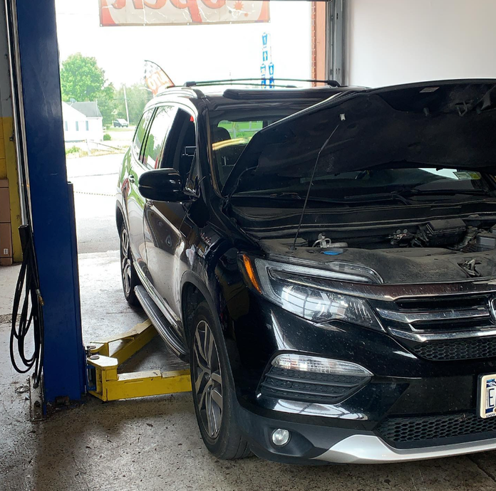 Black SUV with the hood open on a yellow lift inside a garage.