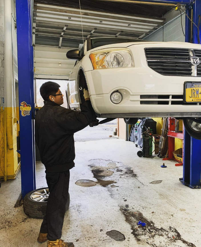 Mechanic working on a white car lifted on a hoist inside a garage.