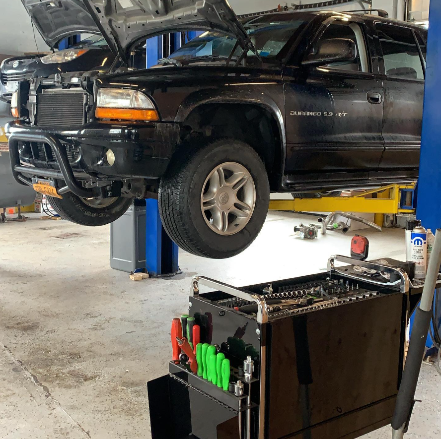 Black SUV on a lift in a garage with tools and open hood.