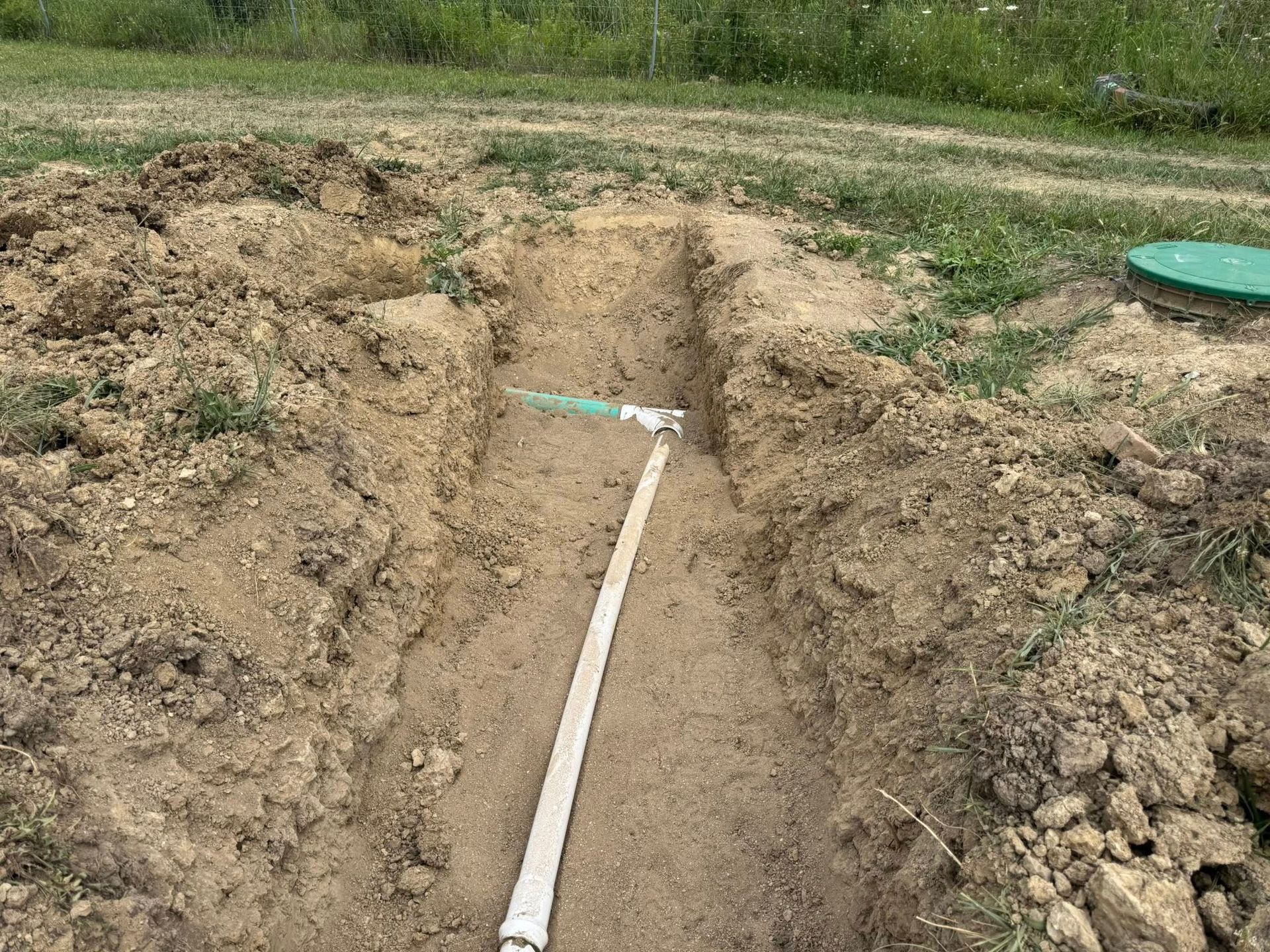 Trench with a white PVC pipe laid in the soil at a construction site.