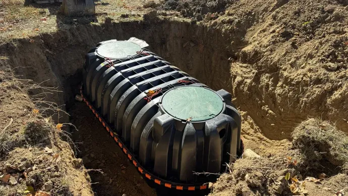 Black plastic tank buried in a dirt trench, topped with white lids and red straps.