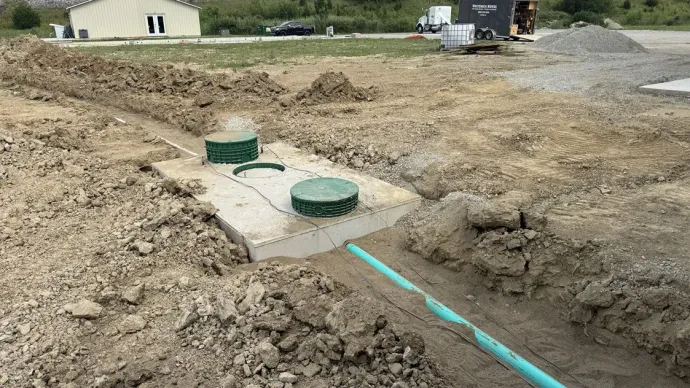 Construction site with two green utility covers and exposed dirt trench beside blue piping