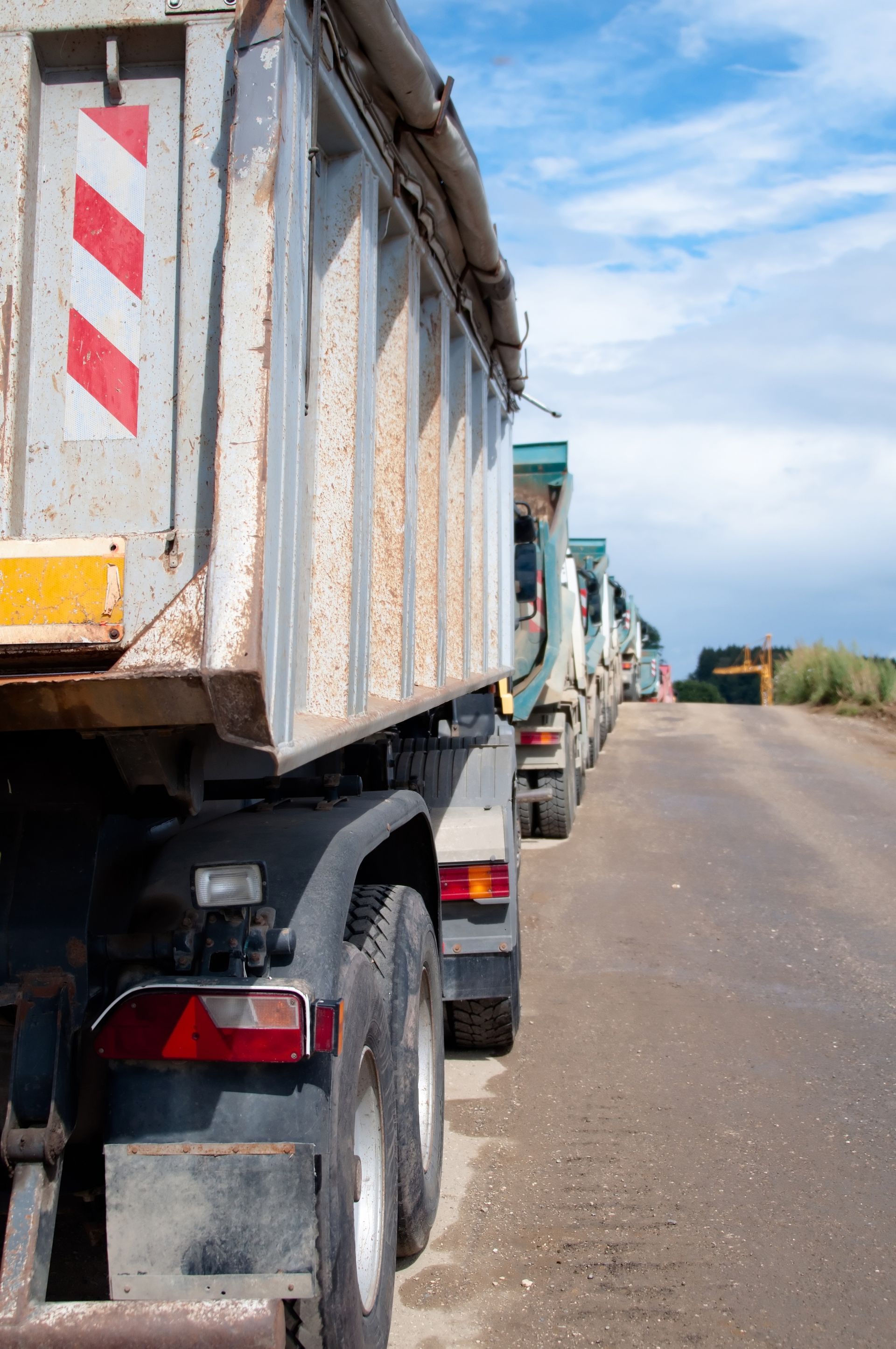 Une rangée de camions-bennes alignés sur une route poussiéreuse sous un ciel d'un bleu éclatant.