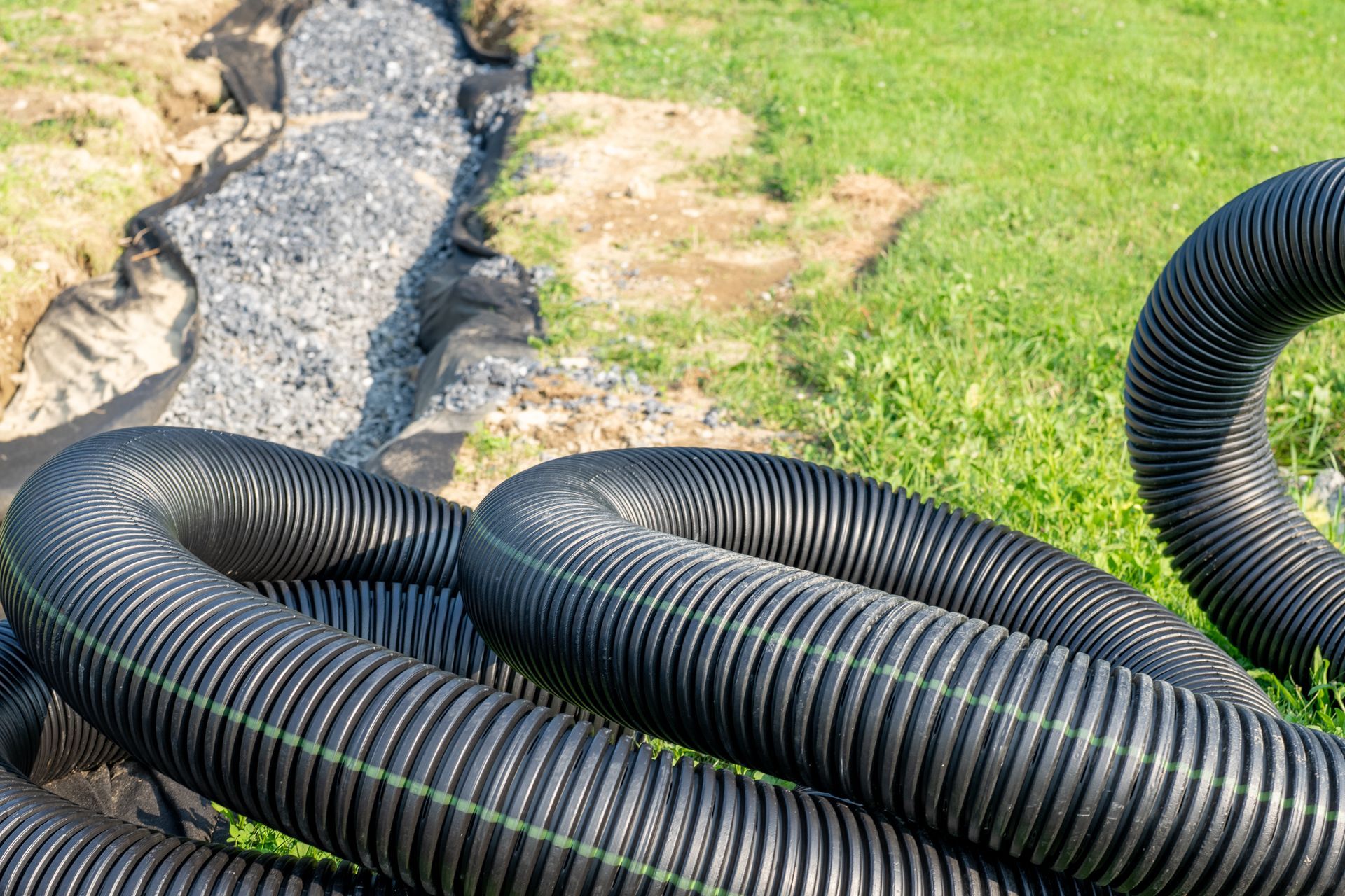 Au premier plan, un tuyau de drainage noir ondulé, et à l'arrière-plan, une tranchée remplie de gravier.
