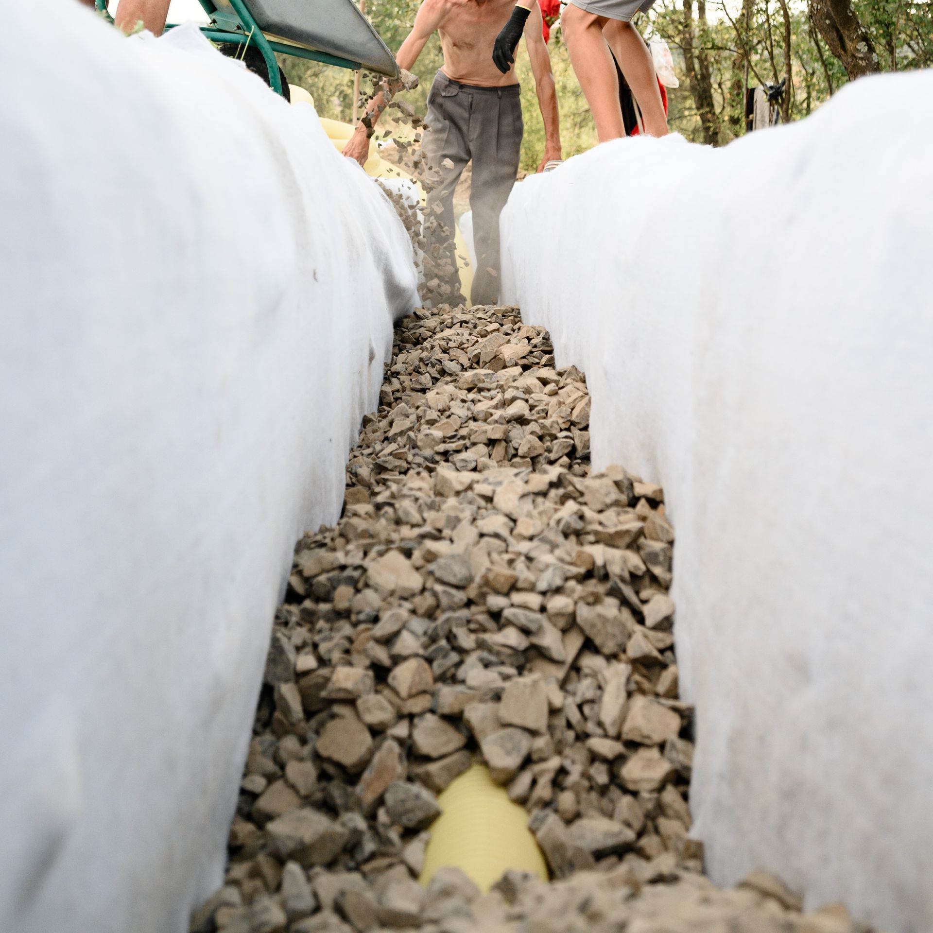 Un tuyau de drainage est installé dans une tranchée tapissée de géotextile blanc et remplie de pierres concassées.