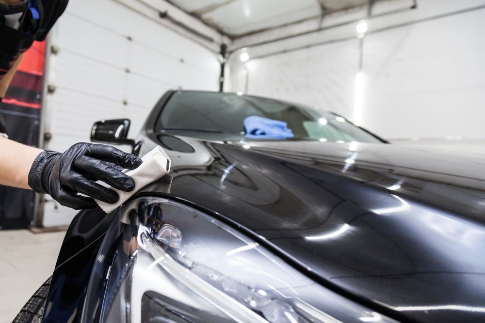 A Person is Polishing the Hood of a Black Car in a Garage — Greg Hennessey Smash Repairs In Woolgoolga, NSW