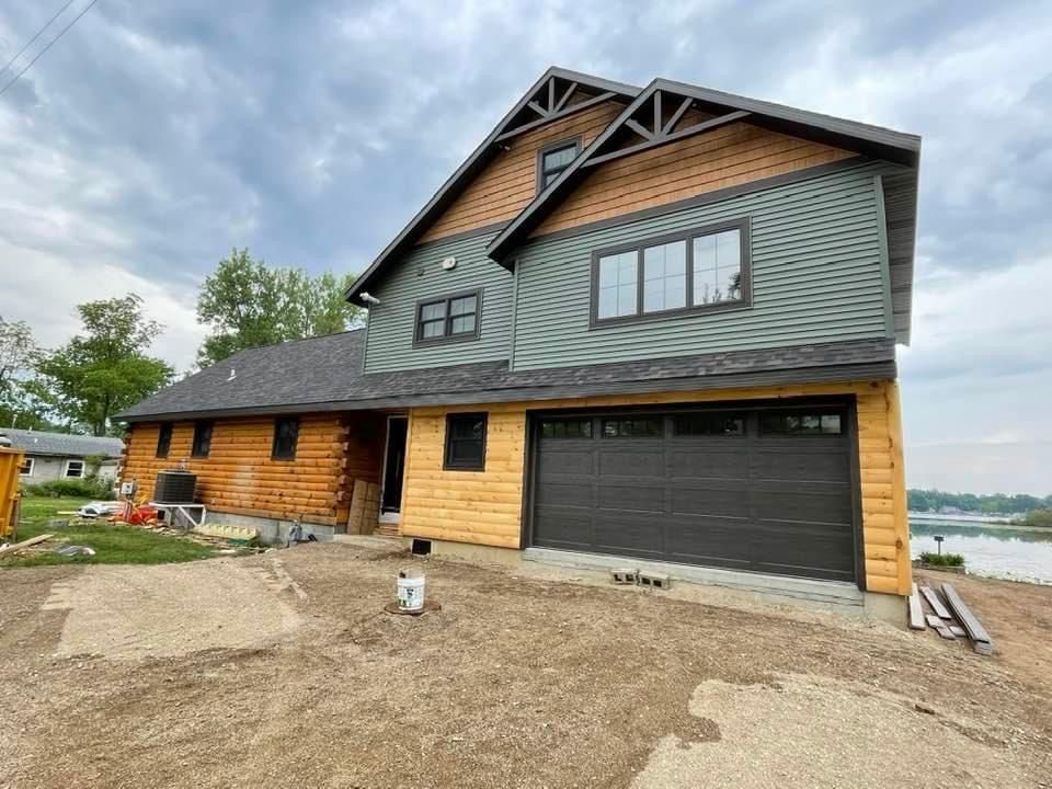 Modern two-story house with dark garage door, wood siding, and lake view under overcast sky