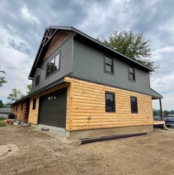 Two-story house with gray siding, log-style lower exterior, and a garage under a cloudy sky.