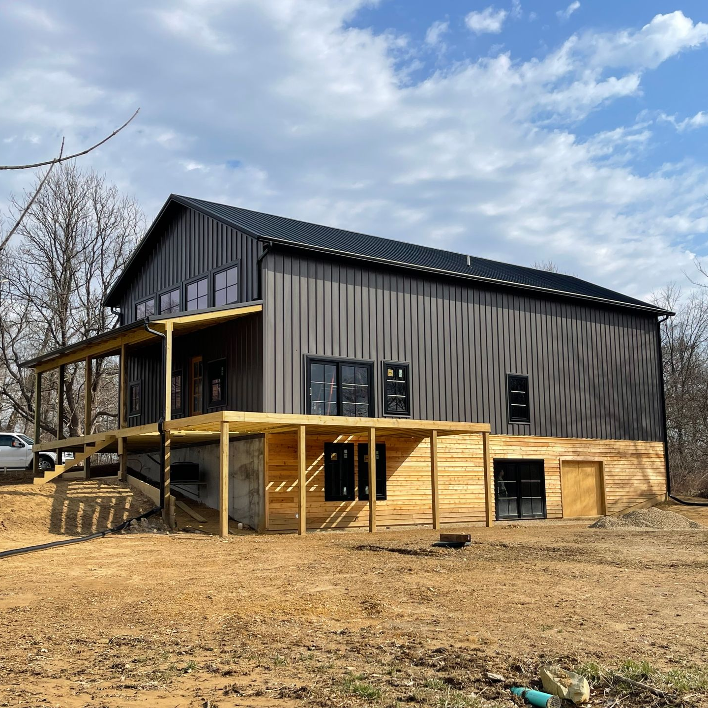 New black-and-wood house with a covered porch on a bare lot under a partly cloudy sky