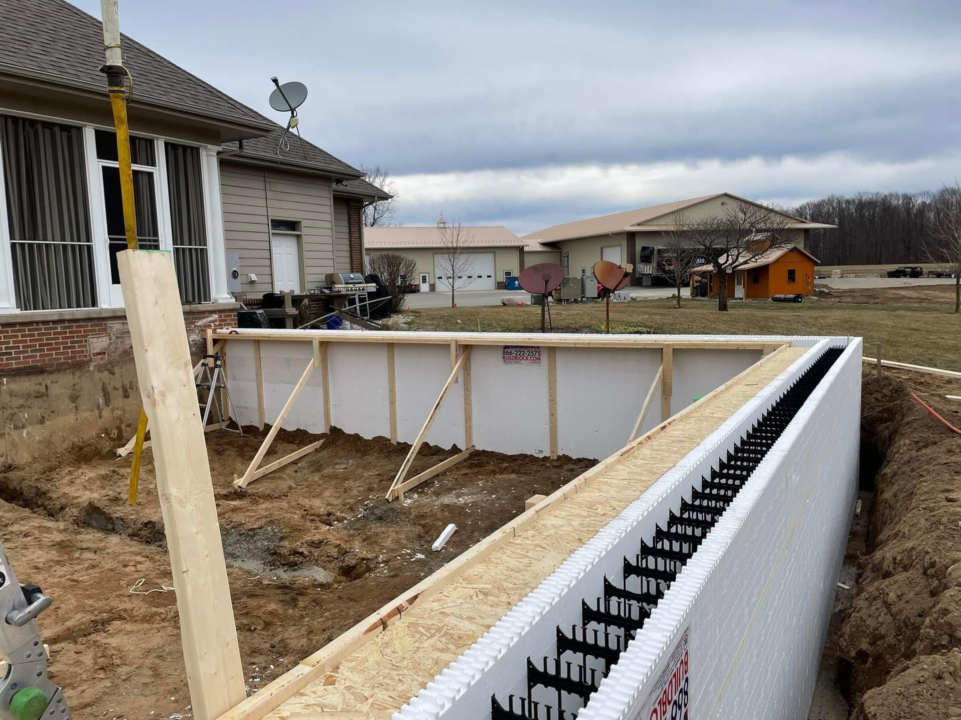 House foundation under construction with concrete wall forms, a white retaining wall, and a muddy yard