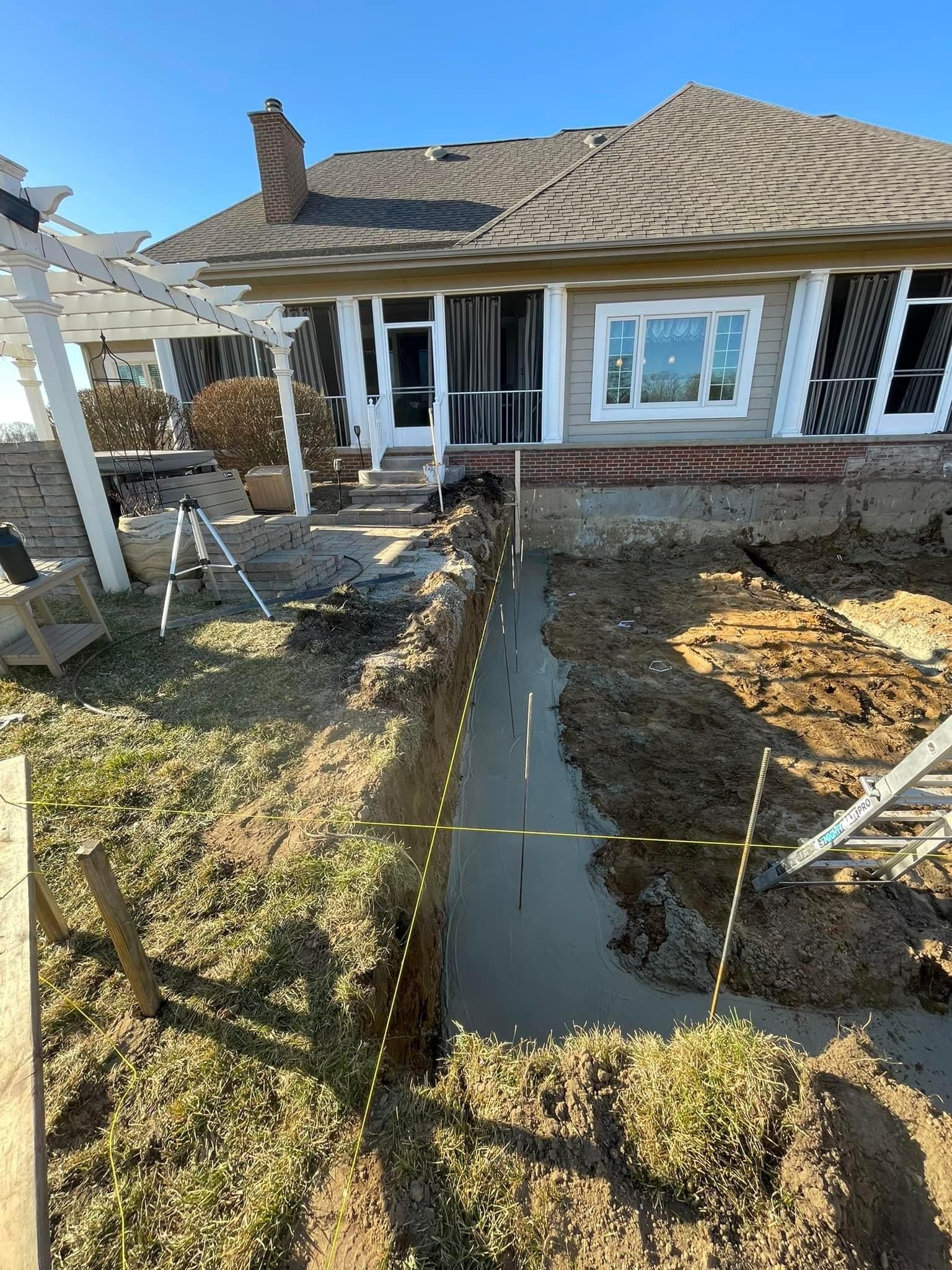 Front yard trench with standing water beside a brick house and window; landscaping work in progress.