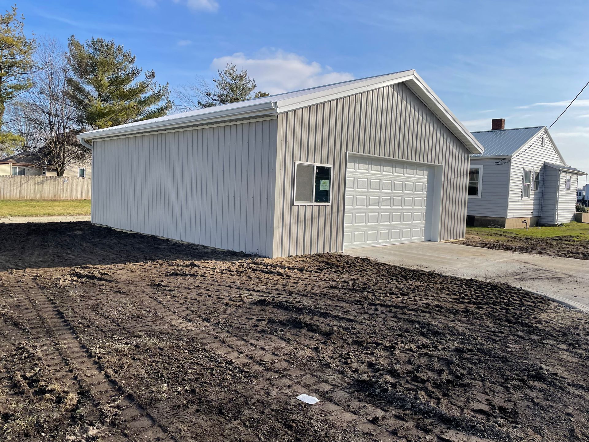 White metal garage with a large overhead door on a muddy lot under a blue sky