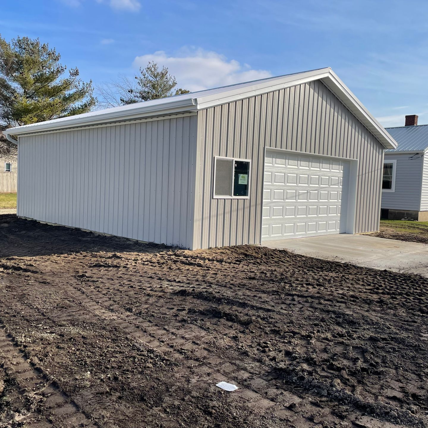White metal garage or shed with a white overhead door on a muddy lot under a clear sky