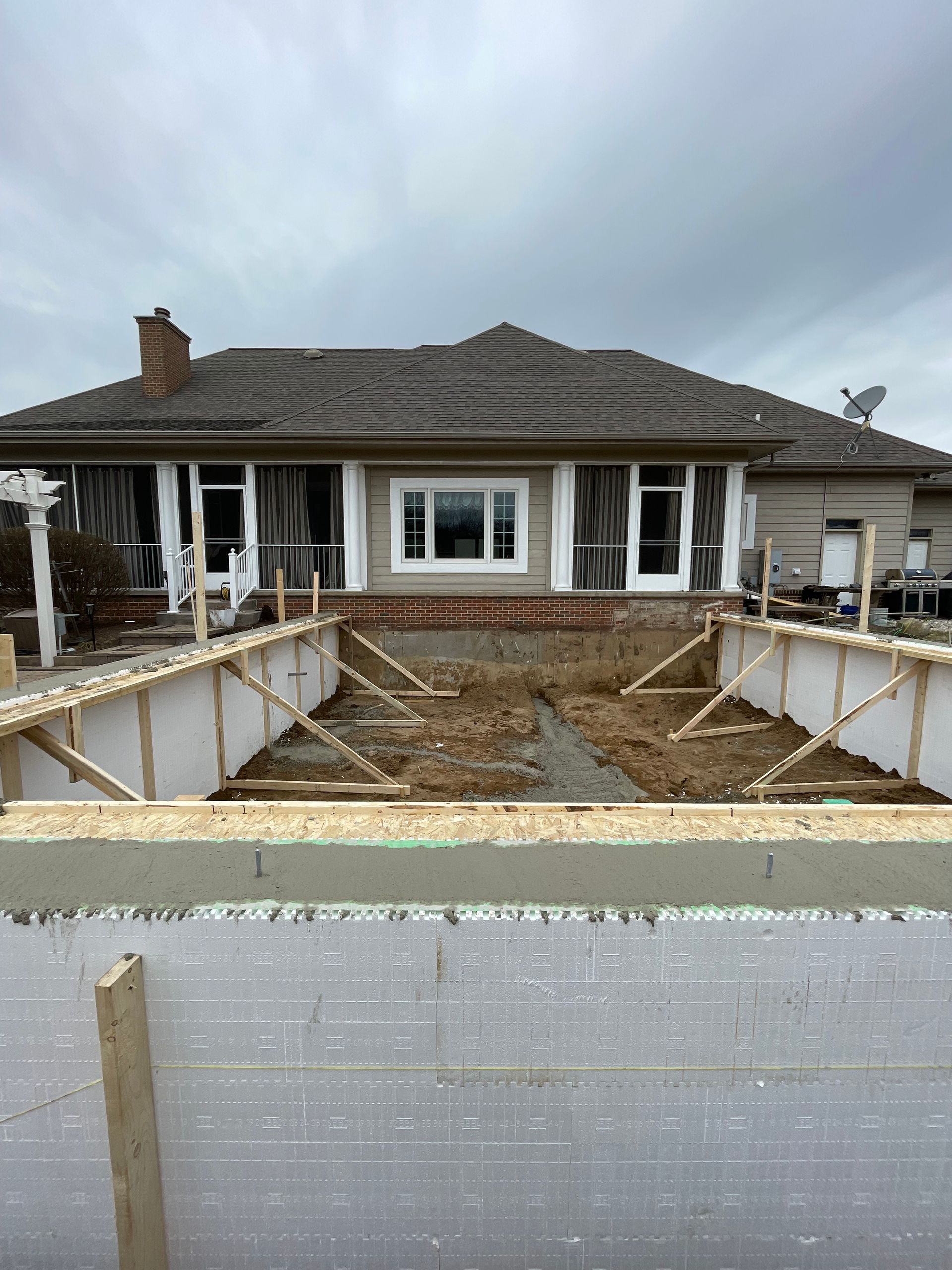 Partially built front yard patio and retaining walls in front of a single-story house under a cloudy sky