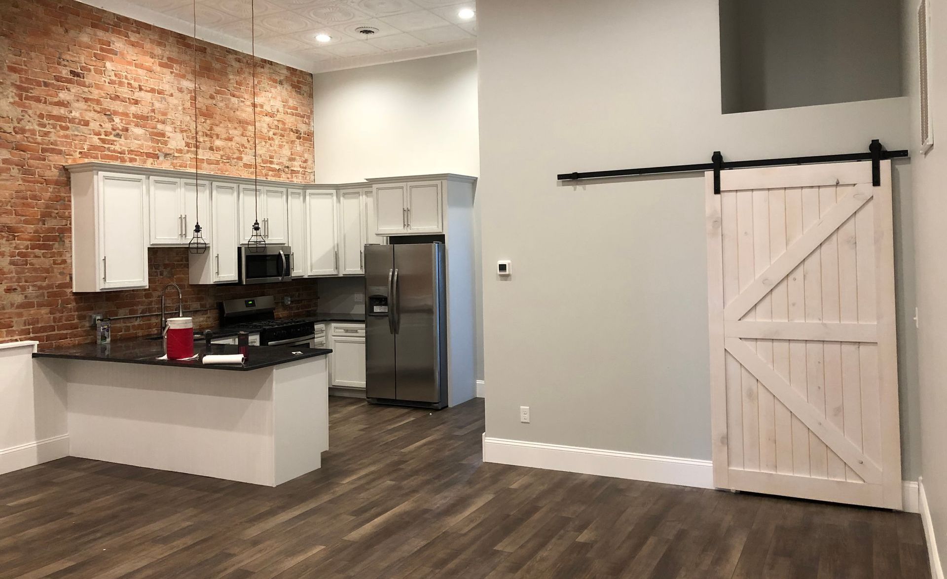 Open kitchen and living area with white cabinets, brick accent wall, dark floors, and a sliding barn door.