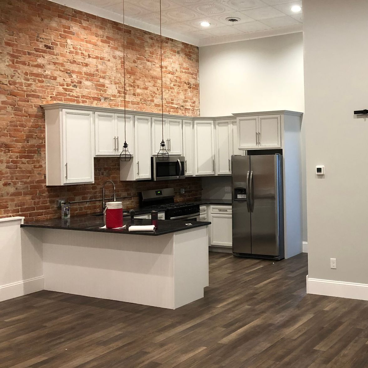 Modern kitchen with white cabinets, brick accent wall, black countertops, and stainless steel refrigerator