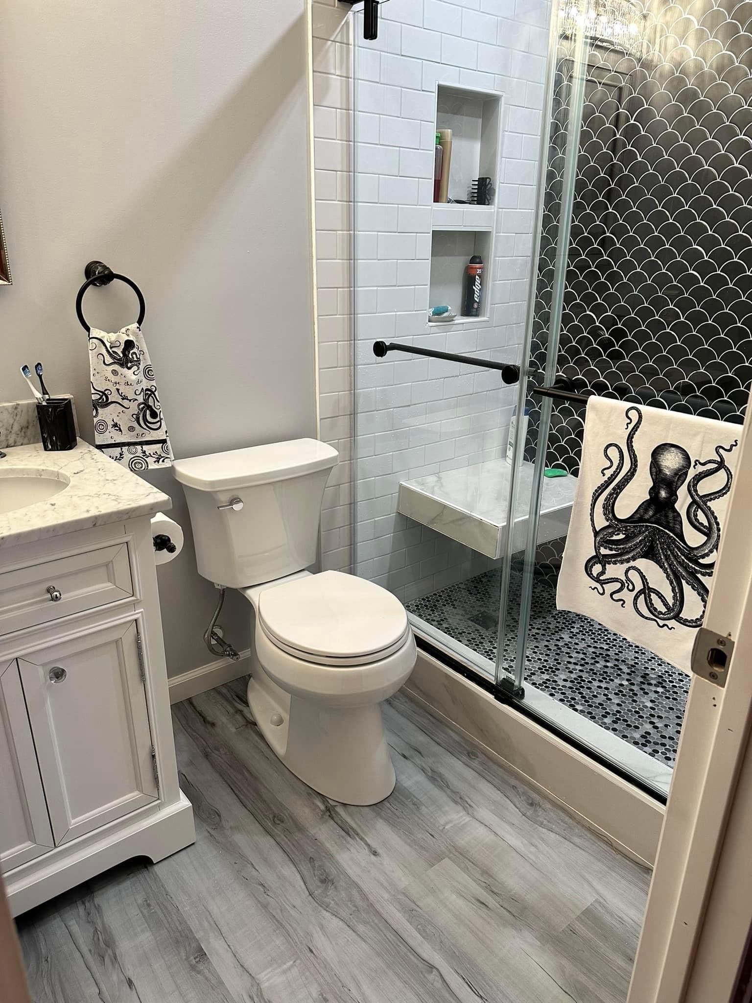 Small bathroom with white toilet, vanity, glass shower, and gray wood-look floor.