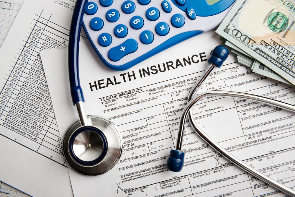A stethoscope , calculator , and money are on top of a health insurance form.