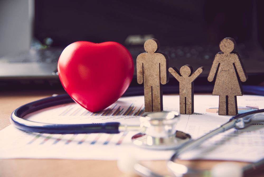 A red heart , wooden figures of a family and a stethoscope on a table.
