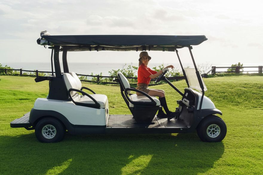 A woman driving a golf cart on a lush green field.