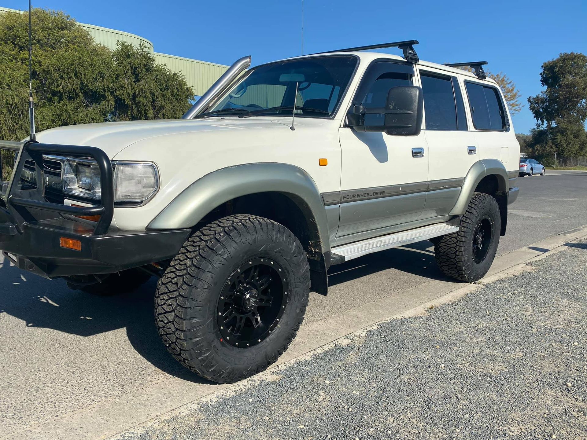 White Car With Black Off-Road Tires Parked On A Gravel Surface
