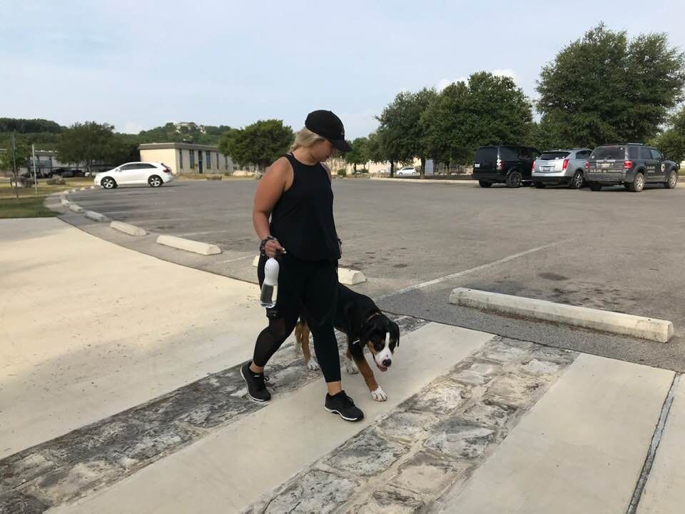 A Woman Walking A Dog On A Leash In A Parking Lot