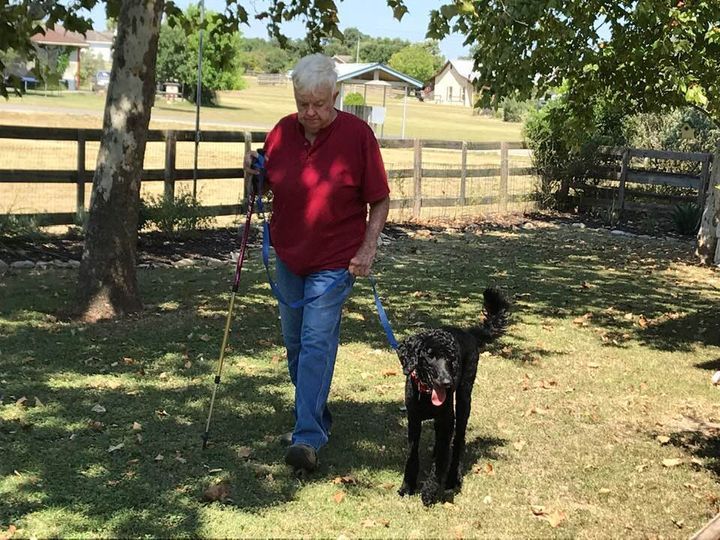 A Man In A Red Shirt Is Walking A Black Dog On A Leash
