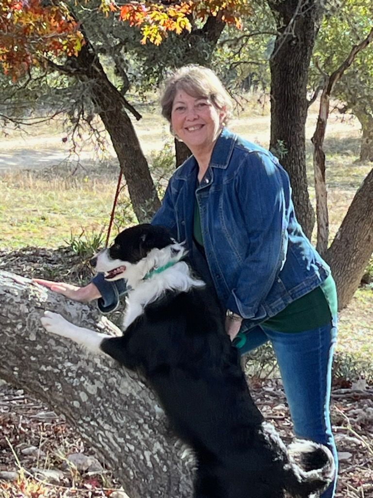 A woman is standing next to a black and white dog on a tree branch.