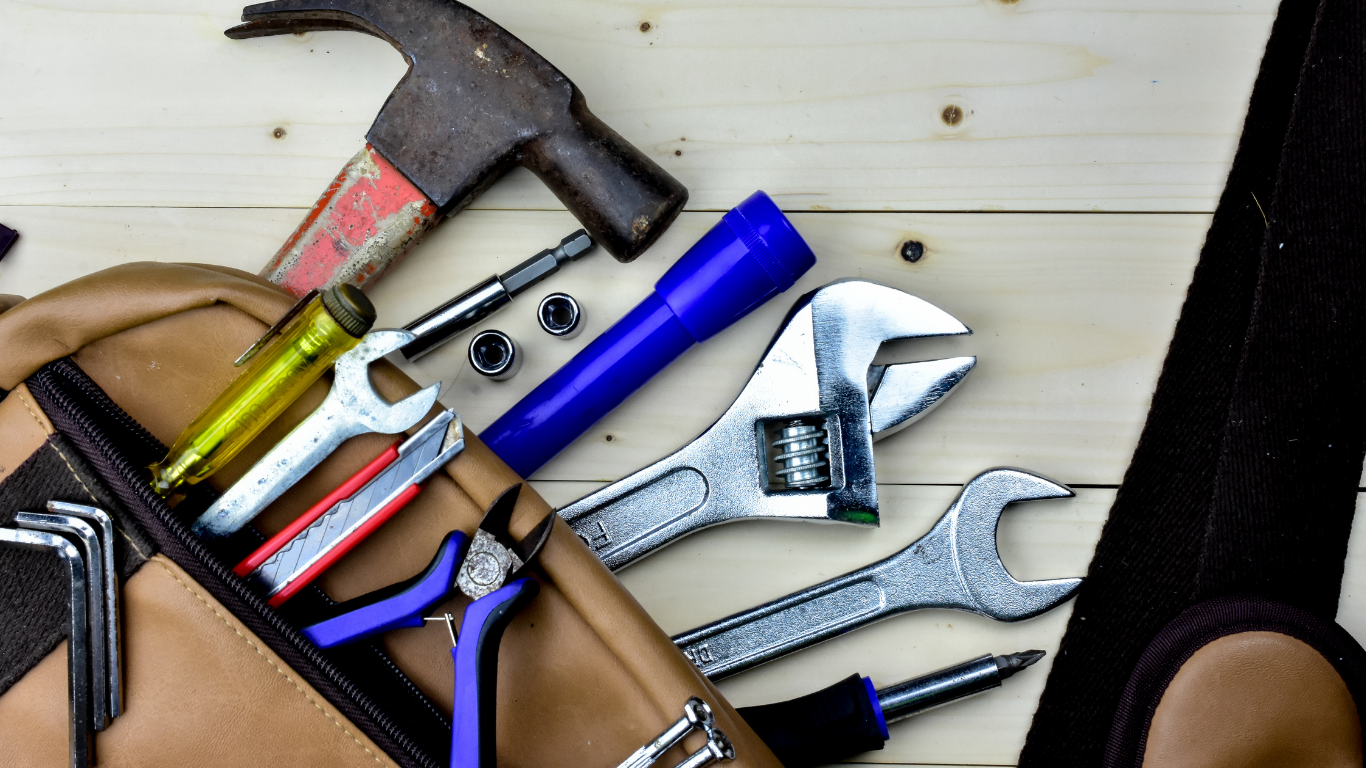 Assorted hand tools, including a hammer, pliers, and wrenches, arranged on a light wooden surface.