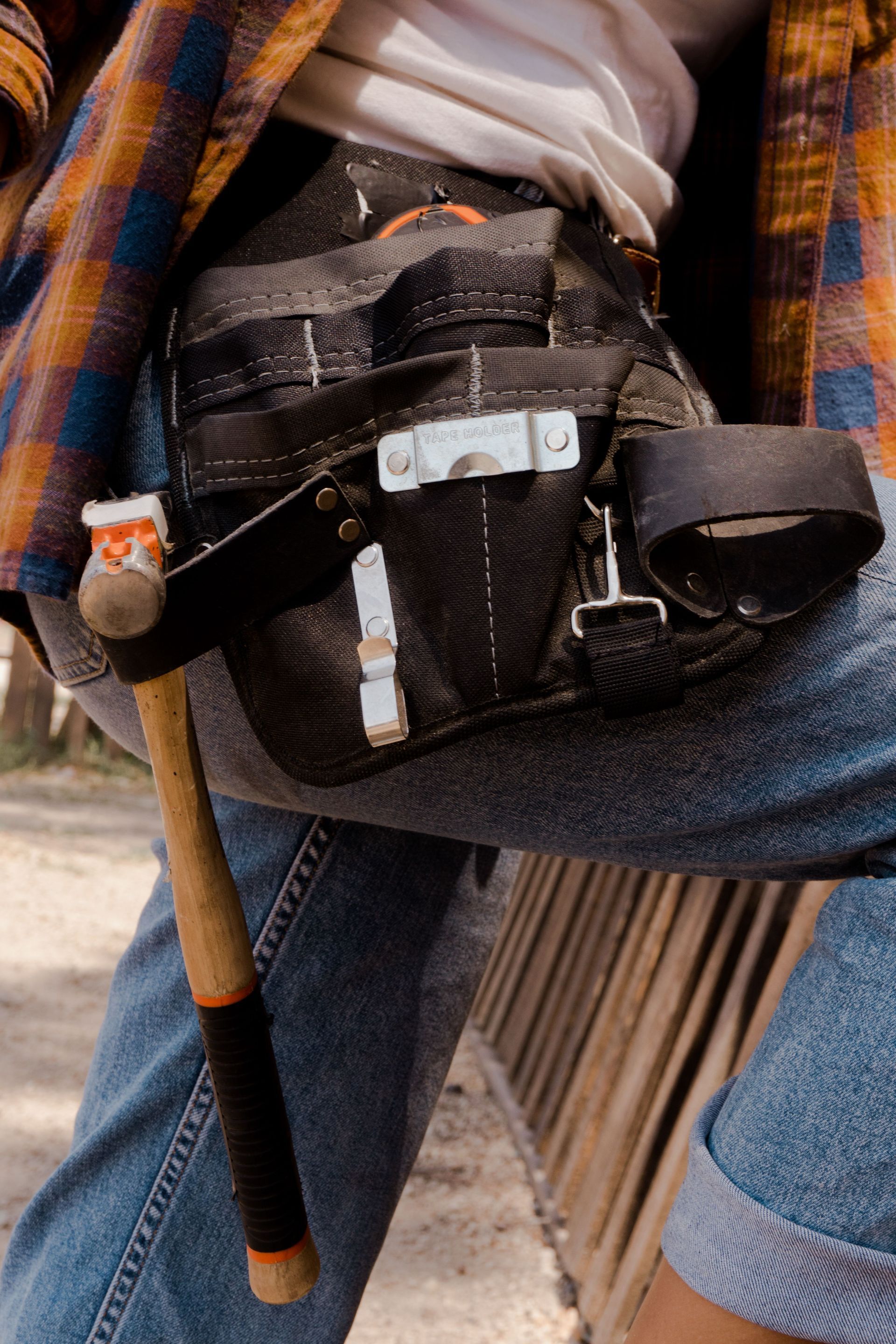 Close-up of a black waist pouch with tools, resting on denim-clad lap beside a wooden cane.