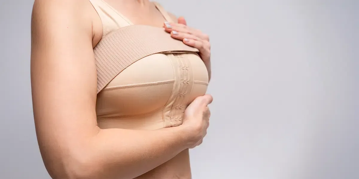 Woman adjusting a beige bra, side view on a light background