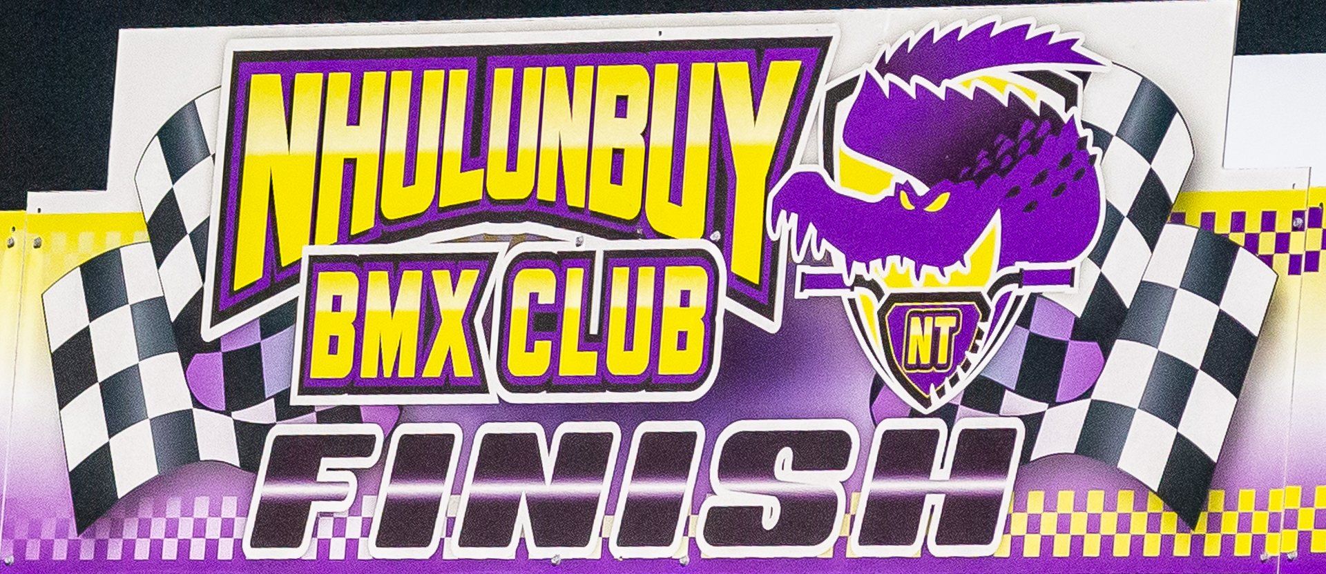 Logo for Nhulunbuy BMX Club, featuring a purple crocodile, checkered flags, and the word