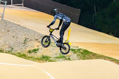 BMX rider in mid-air, performing a jump on a dirt track at night.