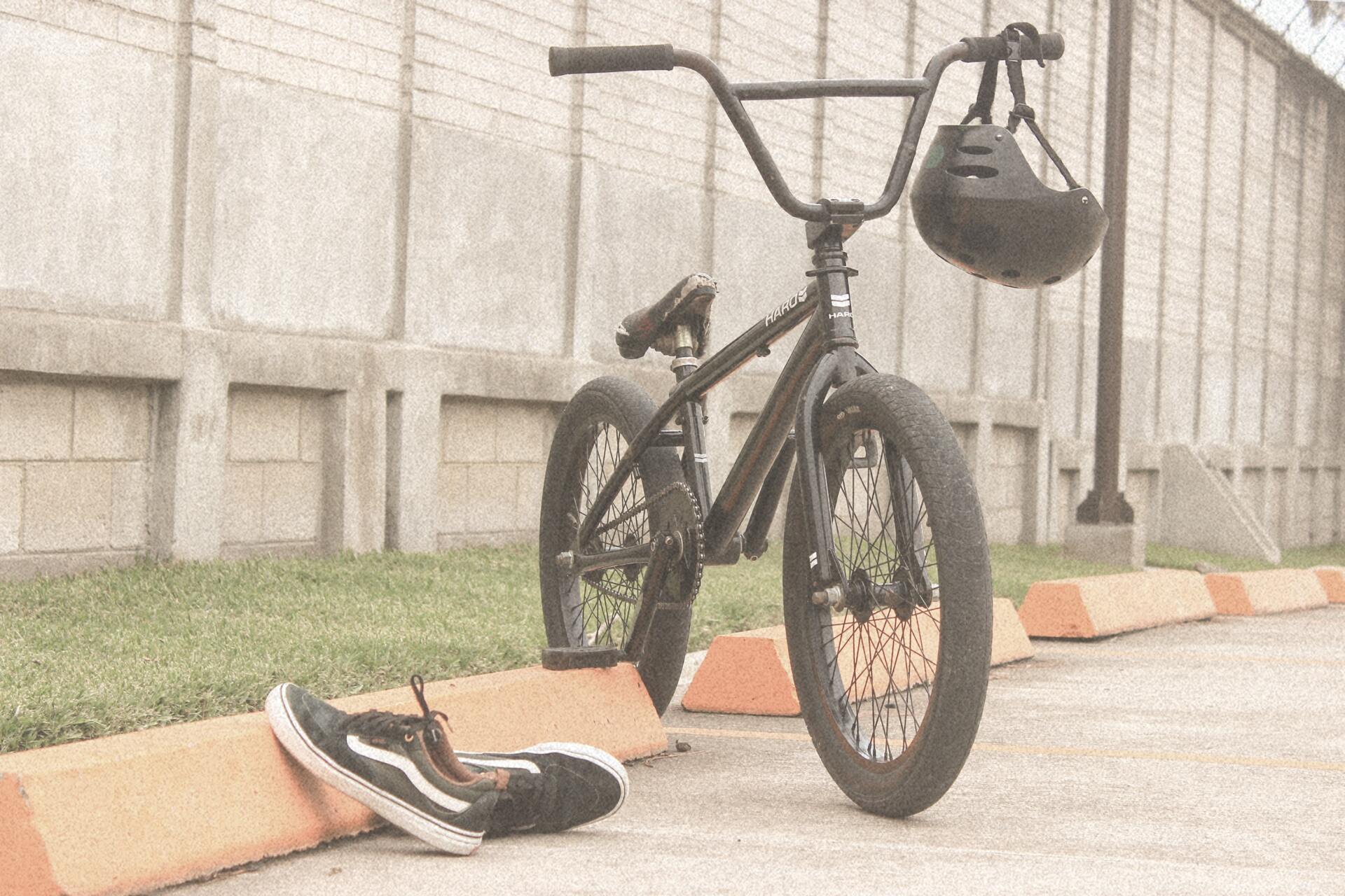 Black BMX bike with a helmet, next to a pair of sneakers, leaning against a wall.