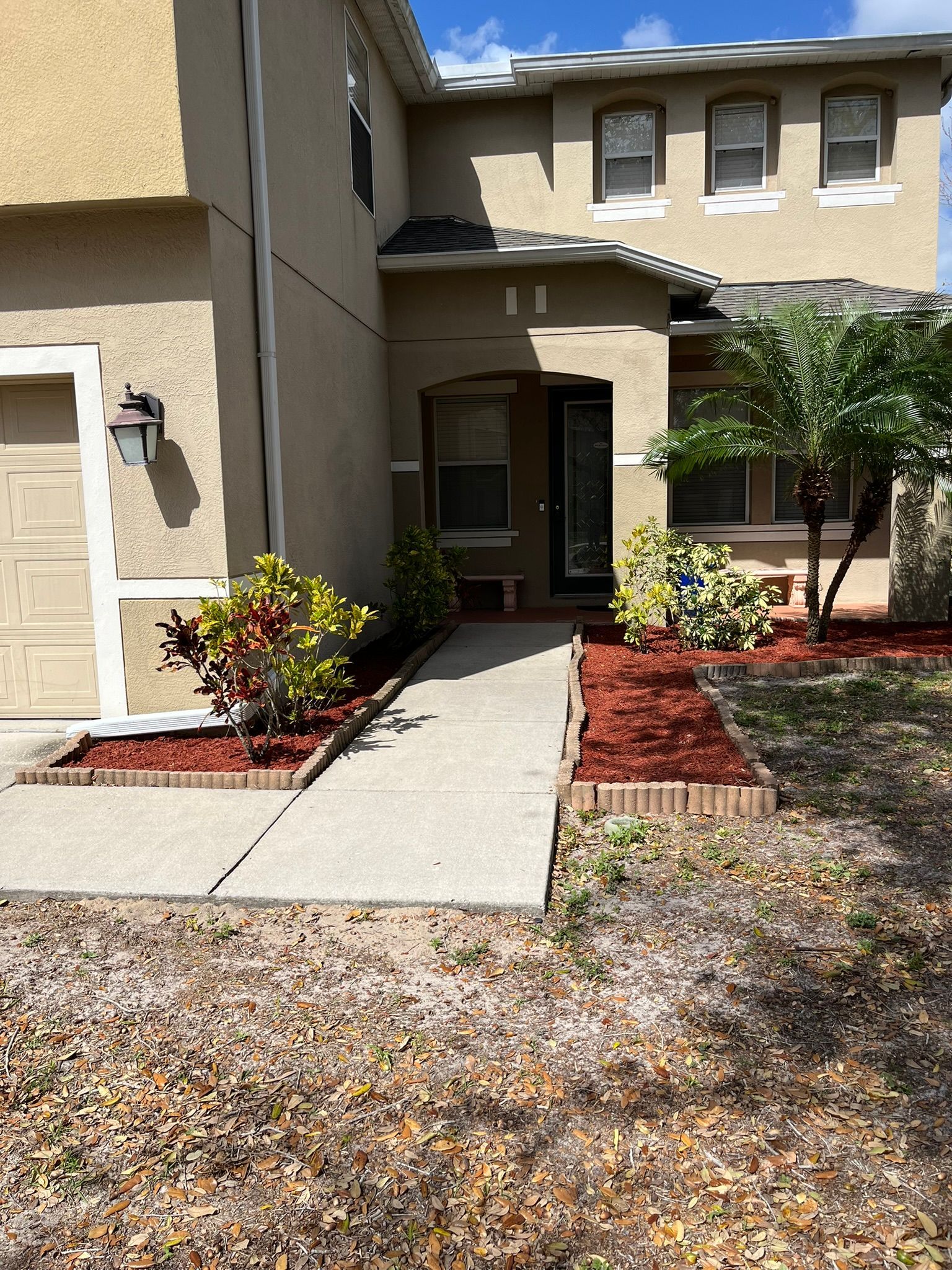 Apartment entrance with tan stucco walls, small covered doorway, and landscaped walkway with red mulch.