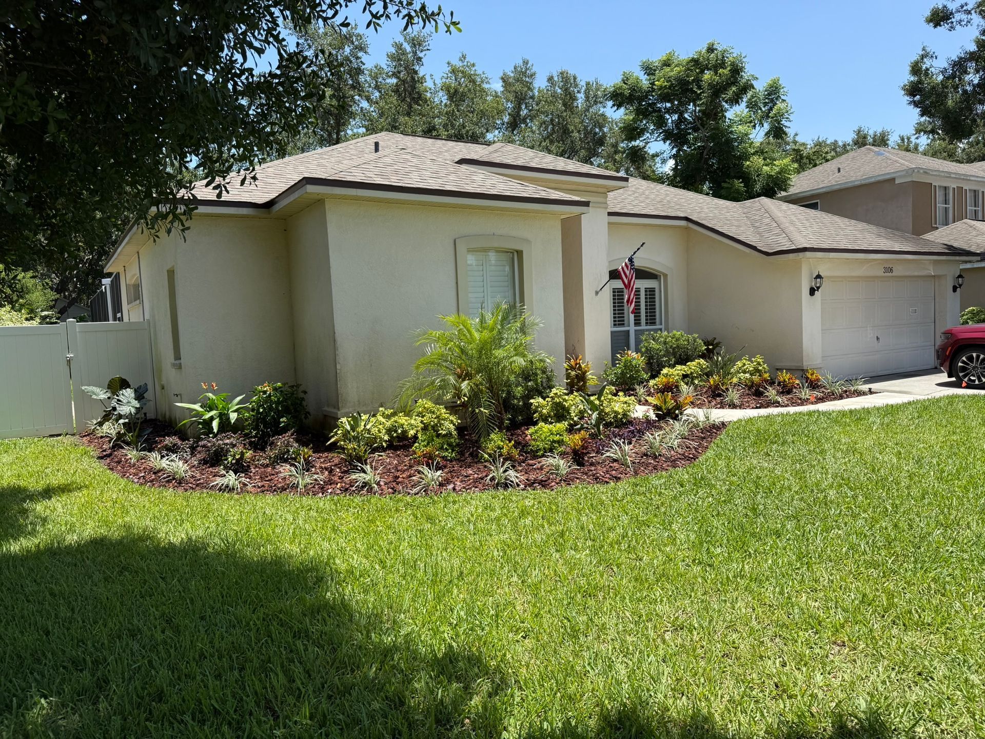Single-story beige house with a tiled roof, front lawn, and landscaped flower bed under a sunny sky