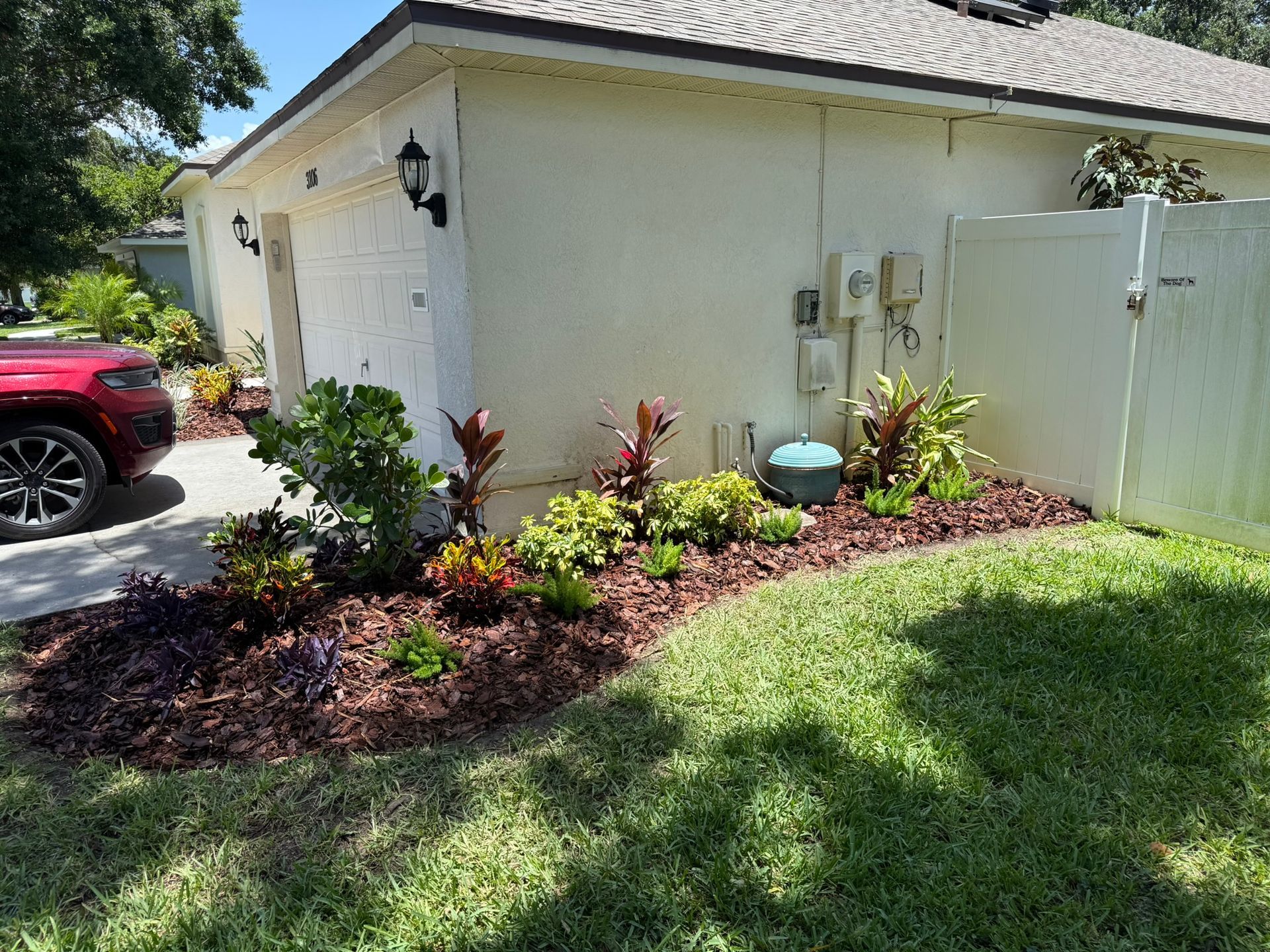 Landscaped front yard with colorful shrubs beside a white house and garage, with a red car parked nearby.