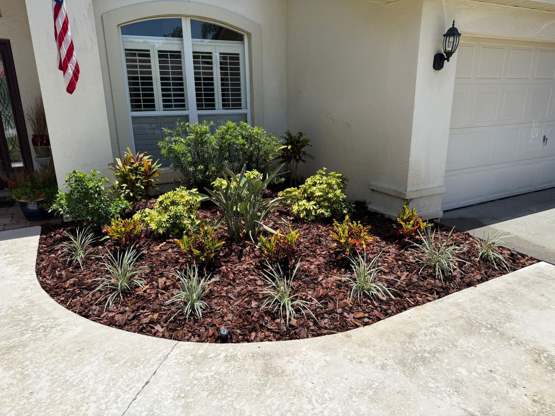 Front yard landscape bed with shrubs and mulch beside a house entry and garage drive