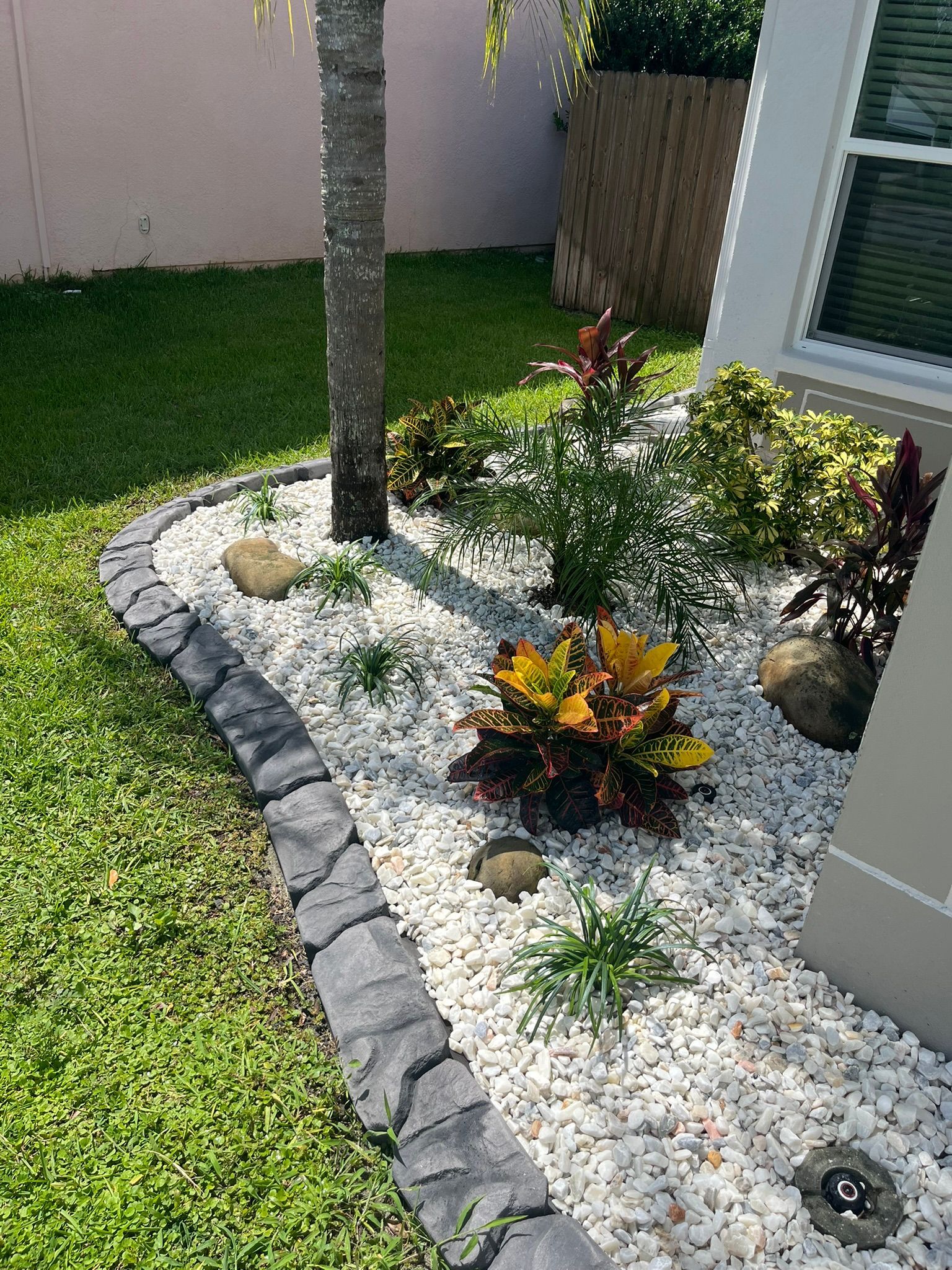 Small landscaped front yard with white gravel, stepping stones, rocks, and a tree beside a house.