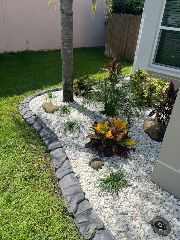 Small landscaped front yard with white gravel, stepping stones, rocks, and a tree beside a house.