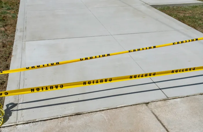 Yellow caution tape blocks a concrete walkway, warning of a hazard.