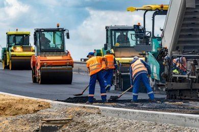 Road construction: Workers paving asphalt with heavy machinery; orange and blue uniforms.