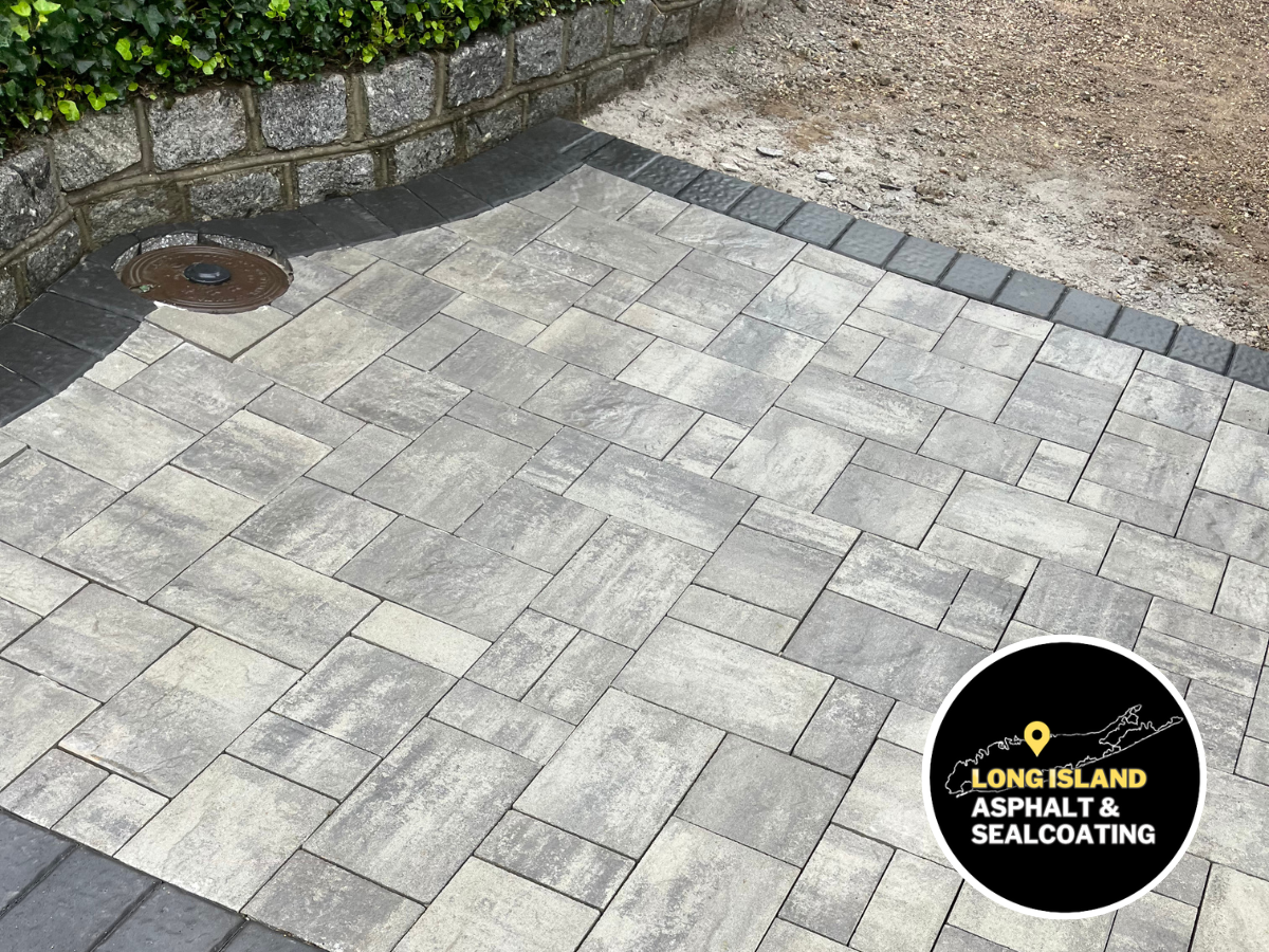 Gray brick pavers on a patio with a retaining wall and a Long Island paving company logo in the corner.