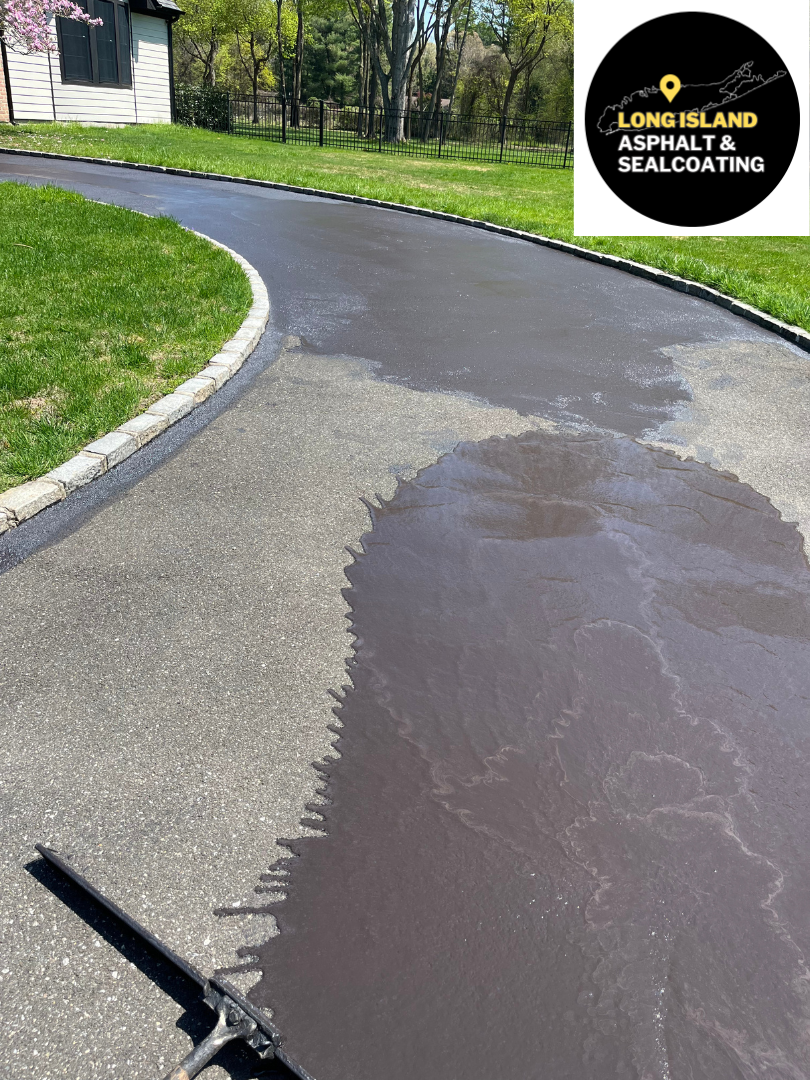 Driveway with sealcoating, showing wet, dark asphalt. Green grass and trees in the background. Company logo in the top right.